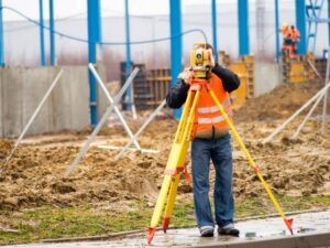 Land surveyor using surveying equipment at a construction site before building layout and construction staking begins