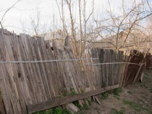 Leaning and deteriorated wooden fence illustrating why a property boundary survey is important before fence replacement.