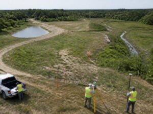 Survey crew mapping a development parcel with drainage areas, a retention pond, and proposed road access in Hialeah, Florida.