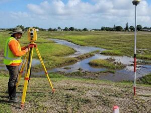 Land surveyor using a total station and GNSS equipment to map drainage patterns on a wet site in Hialeah, Florida.